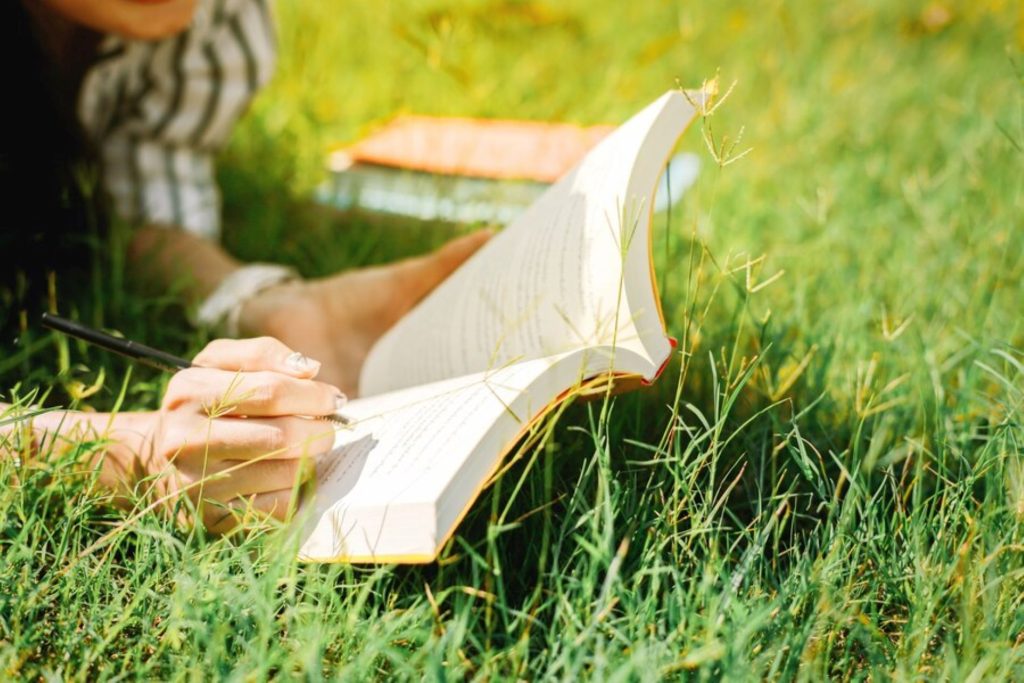cierrese-encima-mano-asiatica-muchacha-leyendo-libro-hierba-verde-jardin_43957-40